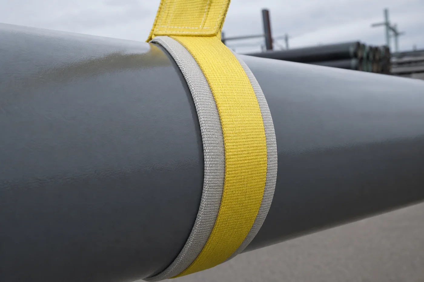 Grey protective sleeve on a yellow pipe lifting strap bearing on a coated steel pipe without marking it